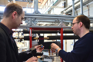  Prof. Dr. Carsten Bäcker (l.) und Stefan Brodale schließen eine Armatur an ihr aufgebautes Trinkwasser-Installationsmodell mit Warm- und Kaltwasserleitung an.  