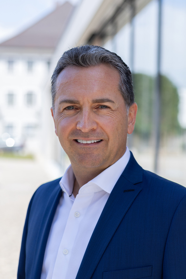 Stefan Grenzebach, in hellblauem Hemd und dunkelblauem Jacket, lächelt in die Kamera.