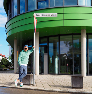 Jan Delay lehnt an Pfosten mit dem Straßenschild der Josef-Grünbeck-Straße.